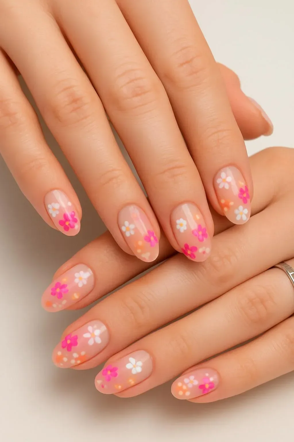 Sheer nude nails adorned with bright pink floral accents for spring 2026 trends.